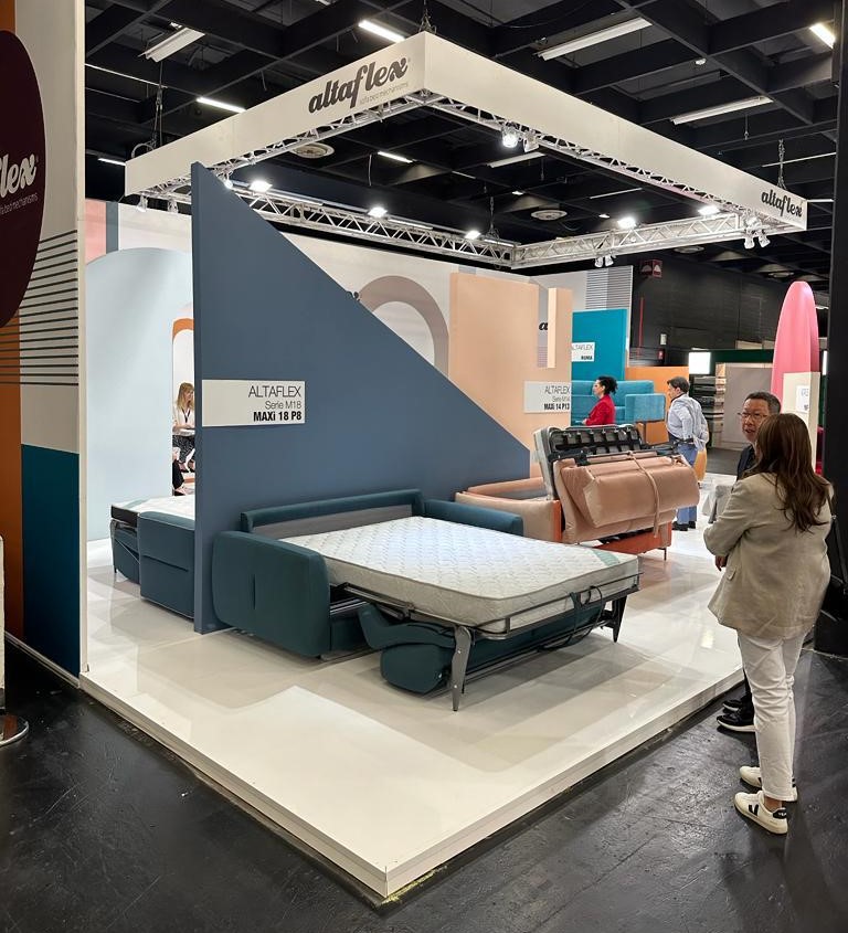 Area espositiva principale dello stand Altaflex Interzum 2023 Colonia - Allestimento professionale con divani letto illuminati da sistema di luci tecniche e appendimenti scenografici