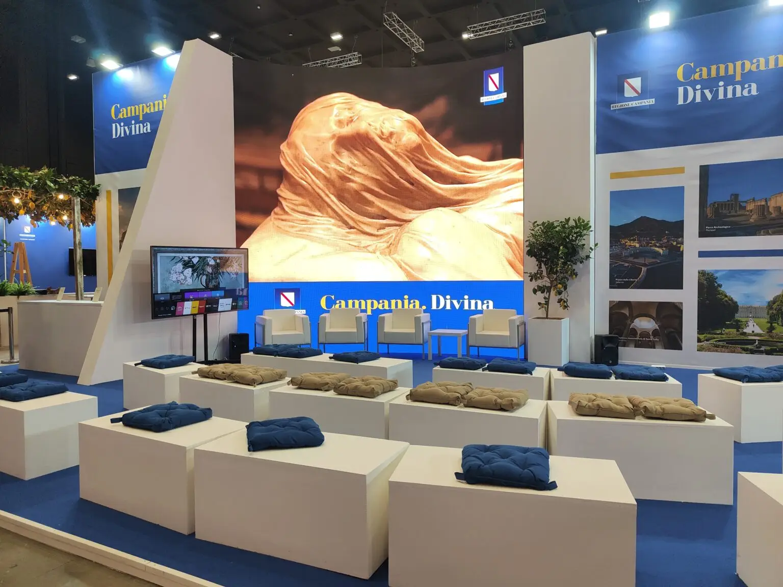 Allestimenti personalizzati per lo stand 'Campania Divina' alla BIT Milano 2024, con un imponente ledwall, piccolo palco per presentazioni, sedute eleganti per espositori e ospiti, e arredi verdi. Un esempio perfetto di allestimento professionale e funzionale