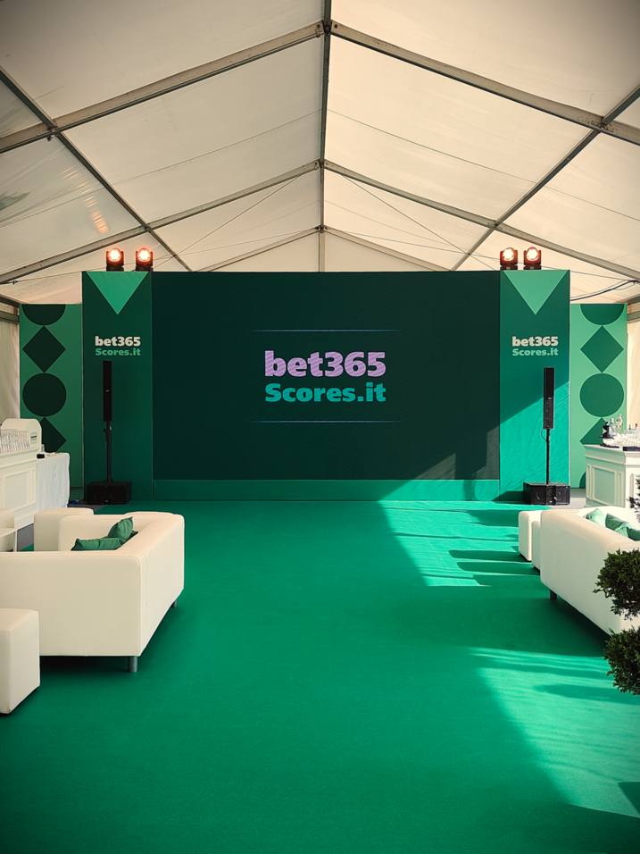 Allestimenti salone per BET 365, con un grande ledwall al centro, illuminazione suggestiva e arredi verdi che valorizzano lo spazio